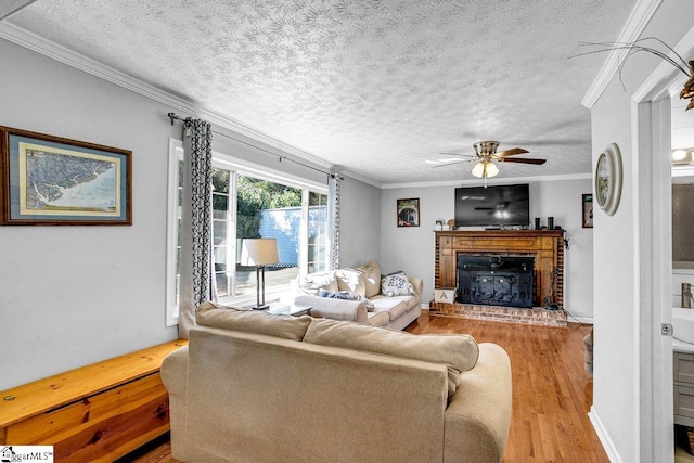 living room featuring a fireplace, light wood-type flooring, ceiling fan, crown molding, and a textured ceiling