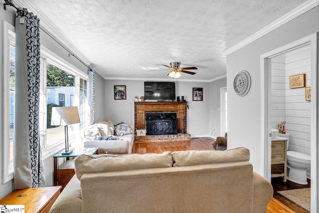 living room featuring hardwood / wood-style flooring, ornamental molding, a brick fireplace, and a textured ceiling