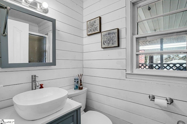 bathroom with walk in shower, wooden walls, vanity, and toilet