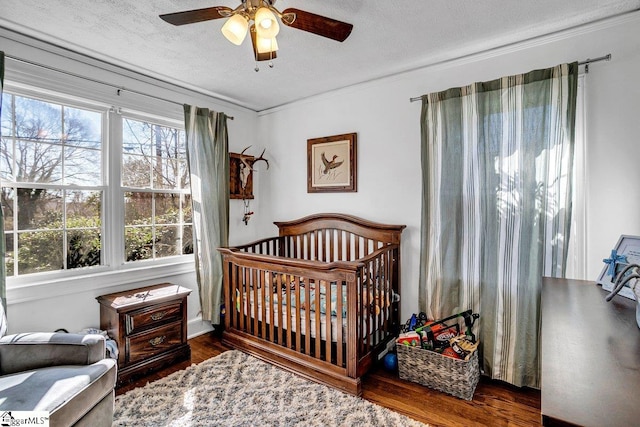 bedroom with ceiling fan, a crib, dark hardwood / wood-style floors, and a textured ceiling