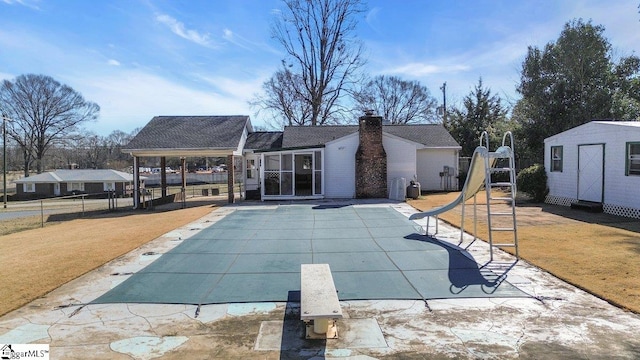 rear view of property with a yard, a patio, a covered pool, and a storage unit