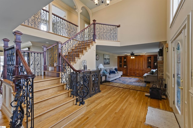 entryway with crown molding, a towering ceiling, wood-type flooring, and decorative columns