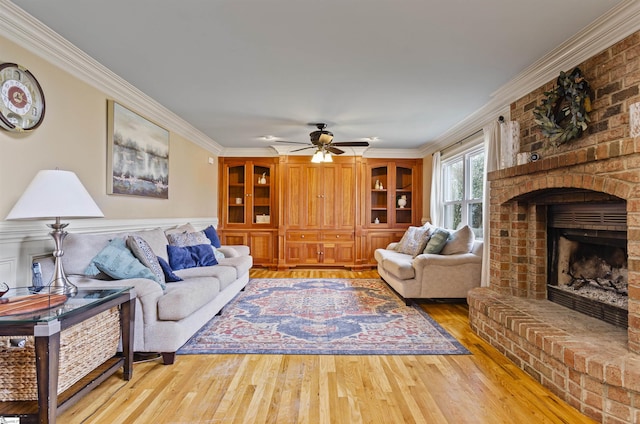 living room with hardwood / wood-style flooring, ceiling fan, ornamental molding, and a brick fireplace