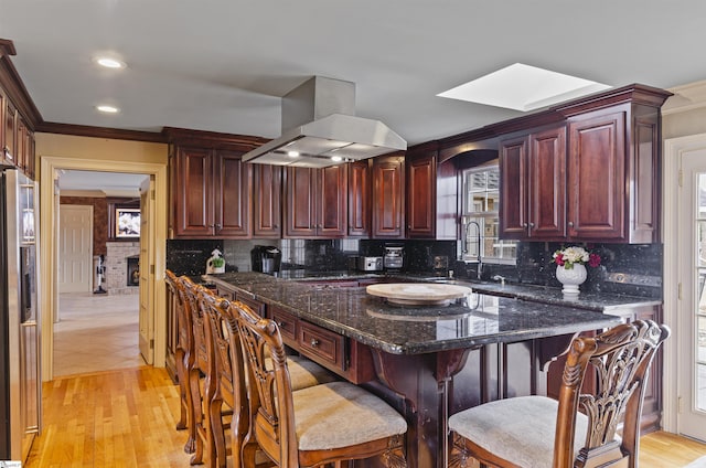 kitchen with sink, crown molding, dark stone countertops, island exhaust hood, and decorative backsplash