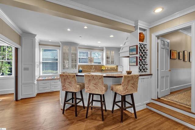 12 Cothran St, Greenville, SC 29605 - kitchen with a kitchen bar, crown molding, tasteful backsplash, light hardwood / wood-style flooring, and white cabinets
