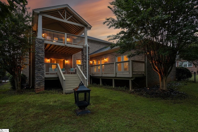 back house at dusk featuring a wooden deck and a yard