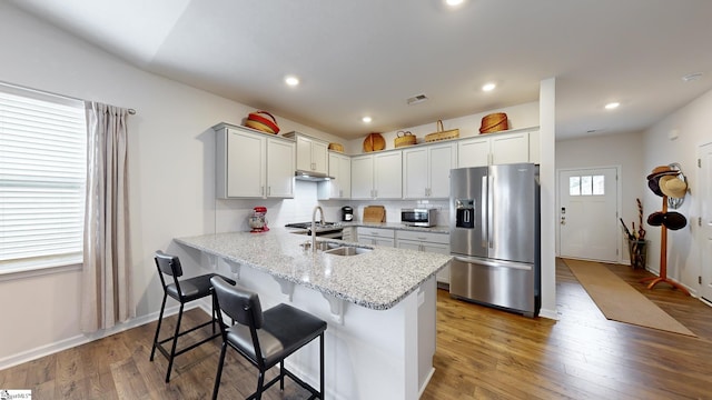 kitchen with appliances with stainless steel finishes, wood-type flooring, a kitchen bar, light stone counters, and kitchen peninsula