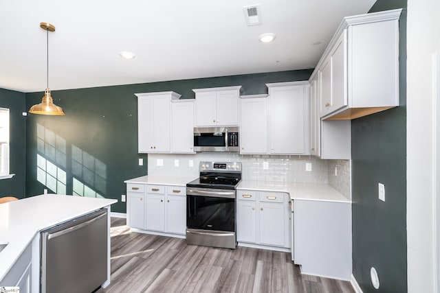 kitchen featuring appliances with stainless steel finishes, pendant lighting, white cabinets, and light hardwood / wood-style flooring