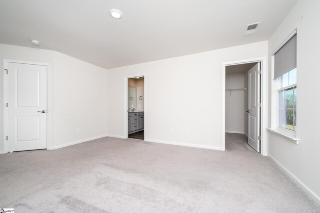 unfurnished bedroom with a closet, ensuite bathroom, a spacious closet, and carpet