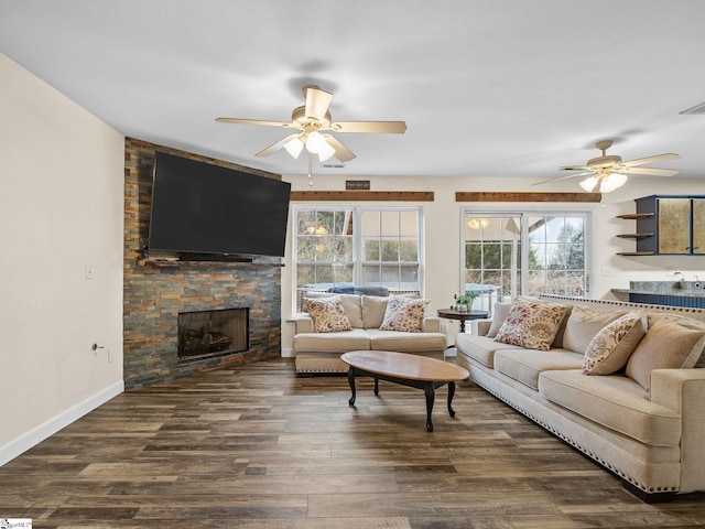 living room with a stone fireplace, dark hardwood / wood-style floors, and ceiling fan