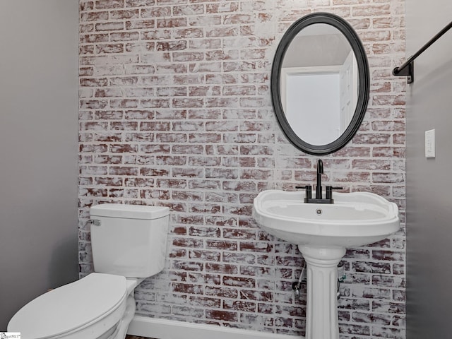 bathroom featuring brick wall and toilet