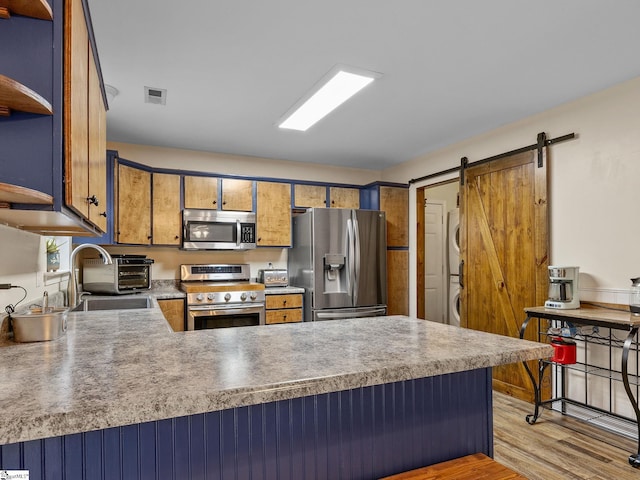 kitchen with stainless steel appliances, a barn door, light hardwood / wood-style floors, and kitchen peninsula