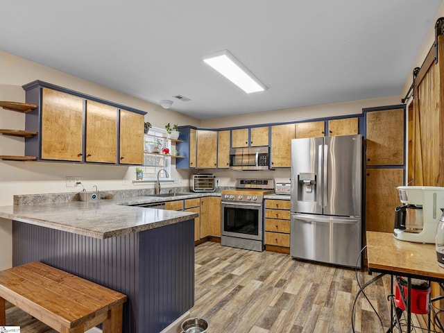 kitchen with sink, stainless steel appliances, kitchen peninsula, a barn door, and light wood-type flooring