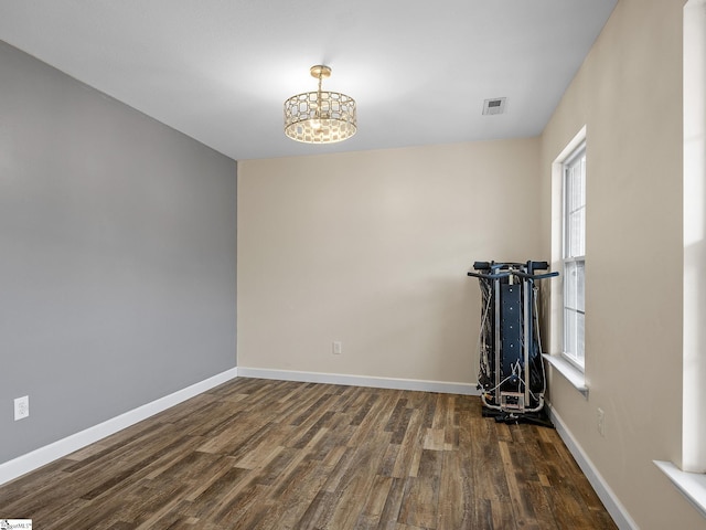 empty room with a notable chandelier and dark wood-type flooring