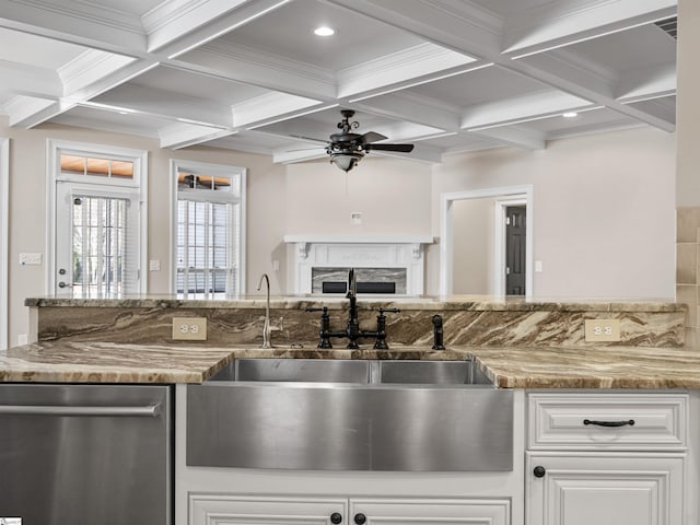 kitchen featuring light stone counters, a fireplace, a sink, stainless steel dishwasher, and beam ceiling