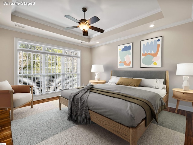 bedroom featuring visible vents, crown molding, a tray ceiling, and wood finished floors