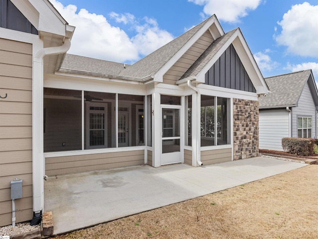 rear view of property featuring a shingled roof, a sunroom, stone siding, board and batten siding, and a patio area