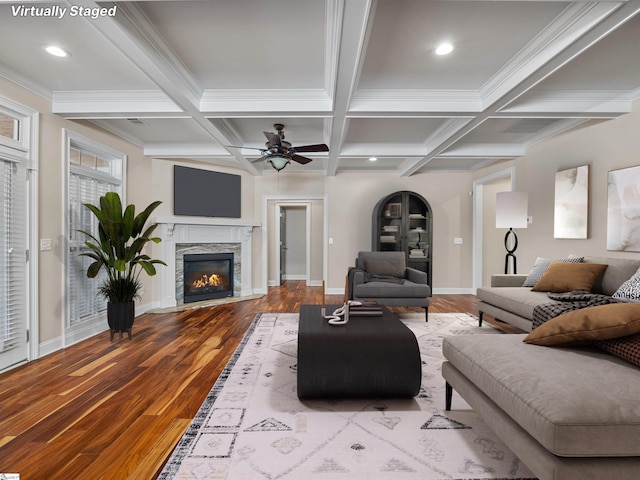 living area featuring baseboards, coffered ceiling, wood finished floors, a stone fireplace, and beam ceiling