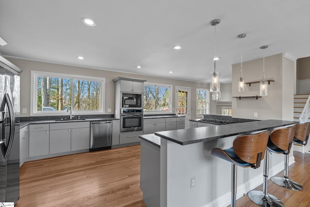 kitchen featuring a breakfast bar, sink, gray cabinetry, hanging light fixtures, and appliances with stainless steel finishes