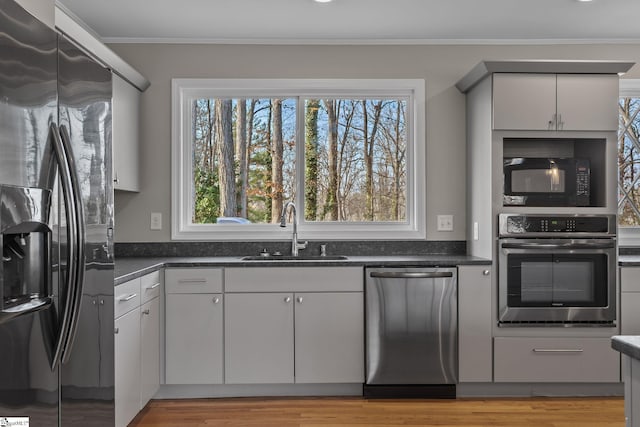 kitchen featuring gray cabinets, sink, stainless steel appliances, crown molding, and light wood-type flooring