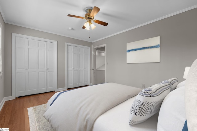 bedroom featuring two closets, wood-type flooring, ornamental molding, and ceiling fan