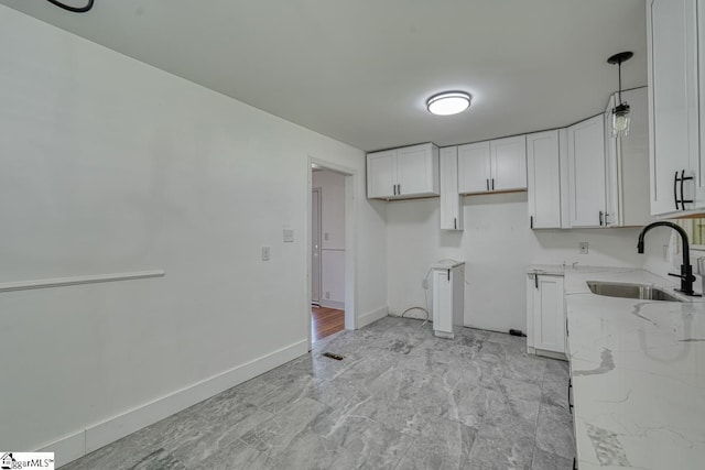 kitchen featuring sink, white cabinets, light stone counters, and decorative light fixtures