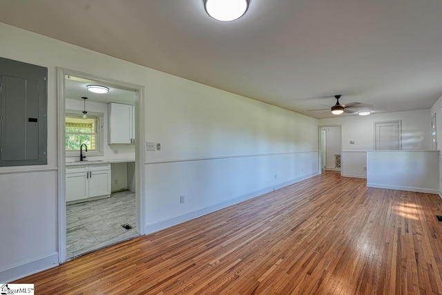 unfurnished room with ceiling fan, sink, electric panel, and light wood-type flooring