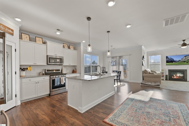 kitchen with white cabinetry, stainless steel appliances, decorative light fixtures, and a kitchen island with sink