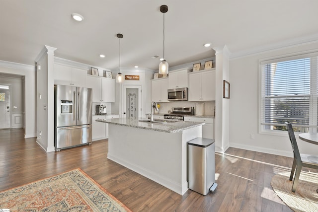 kitchen featuring hanging light fixtures, stainless steel appliances, light stone countertops, an island with sink, and white cabinets