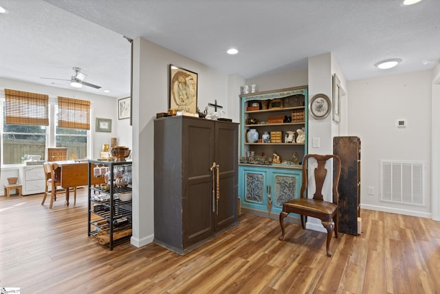 living area with hardwood / wood-style flooring, ceiling fan, and a textured ceiling