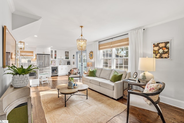 living room featuring an inviting chandelier, hardwood / wood-style floors, crown molding, and beverage cooler