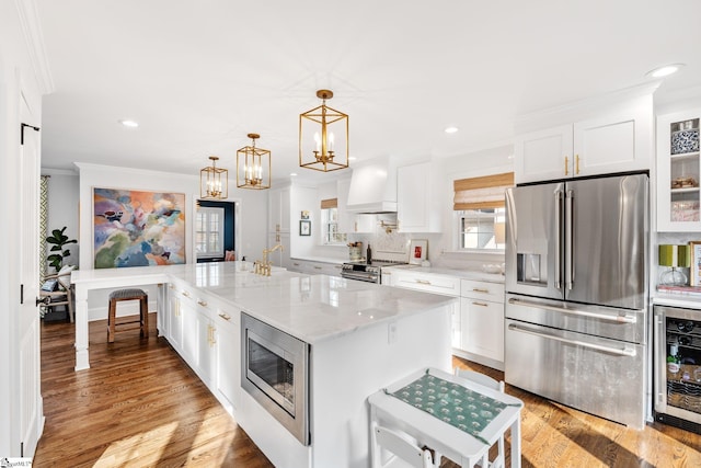 kitchen with wine cooler, white cabinetry, light stone counters, appliances with stainless steel finishes, and a kitchen island with sink