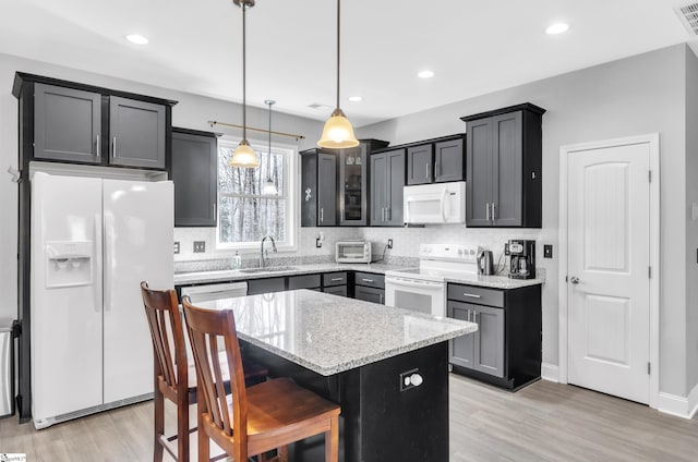 kitchen featuring pendant lighting, sink, white appliances, a center island, and light stone counters