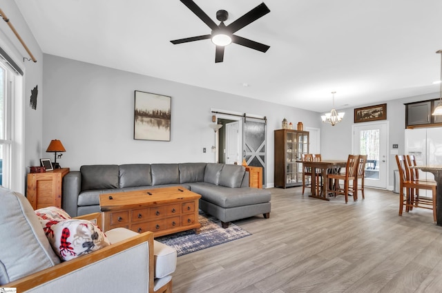 living room featuring a barn door, ceiling fan with notable chandelier, and light hardwood / wood-style floors