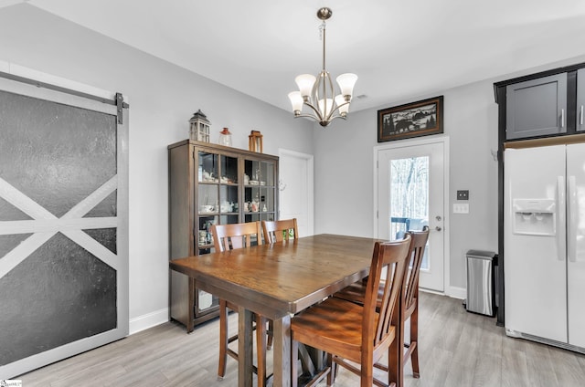 dining space with a barn door, a chandelier, and light wood-type flooring