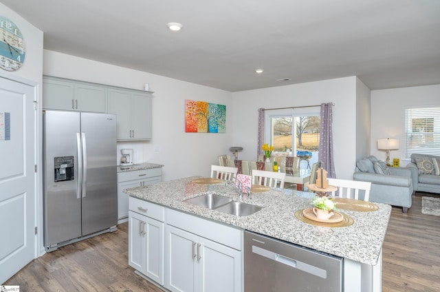 kitchen featuring sink, appliances with stainless steel finishes, an island with sink, hardwood / wood-style flooring, and light stone countertops