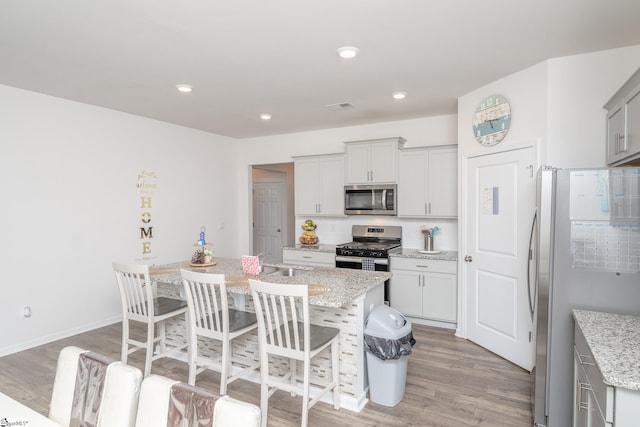 kitchen featuring light stone counters, stainless steel appliances, a kitchen breakfast bar, and a kitchen island with sink