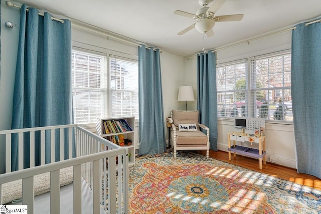 bedroom with wood-type flooring, a nursery area, and ceiling fan