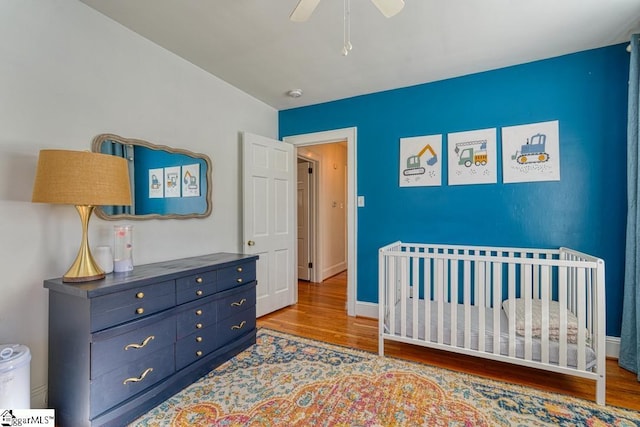 bedroom with wood-type flooring, a nursery area, and ceiling fan