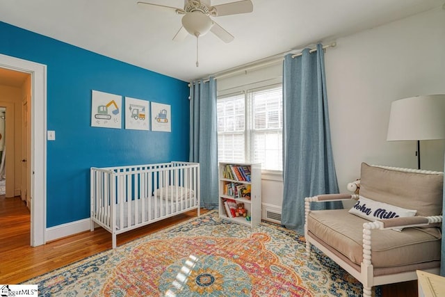 bedroom with hardwood / wood-style flooring, ceiling fan, and a crib