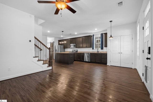 kitchen with appliances with stainless steel finishes, decorative light fixtures, sink, a center island, and dark wood-type flooring