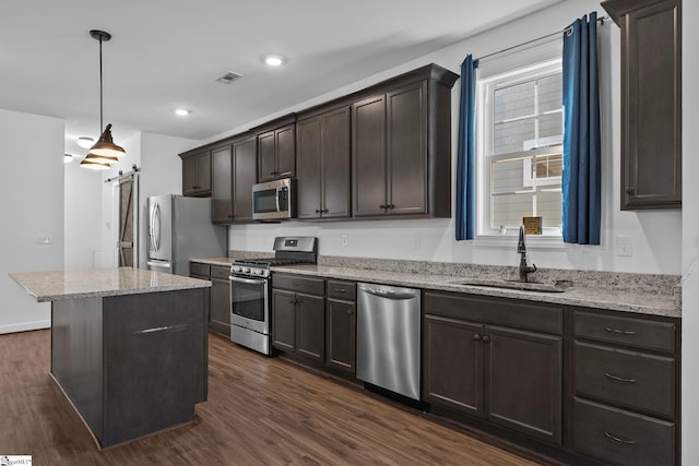 kitchen with a kitchen island, appliances with stainless steel finishes, decorative light fixtures, sink, and a barn door