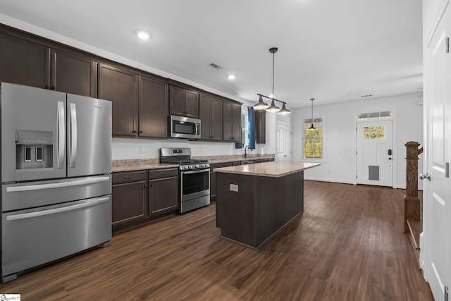 kitchen featuring hanging light fixtures, stainless steel appliances, light stone counters, dark brown cabinetry, and a kitchen island