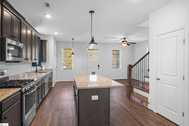 kitchen with pendant lighting, sink, stainless steel appliances, light stone countertops, and a kitchen island