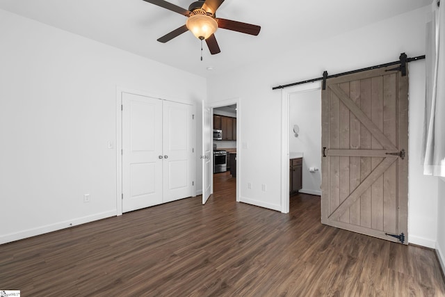 unfurnished bedroom featuring ceiling fan, a barn door, dark hardwood / wood-style flooring, and a closet