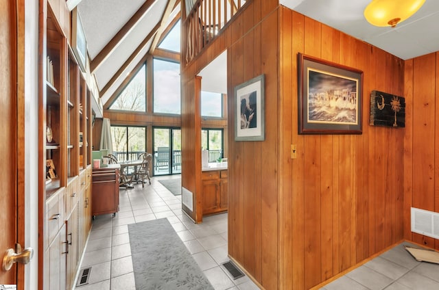 hallway with light tile patterned floors, wooden walls, and high vaulted ceiling