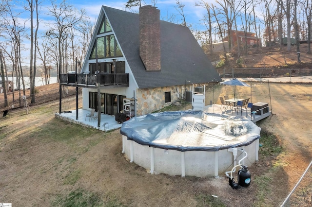 back of property with a patio, a covered pool, and a water view