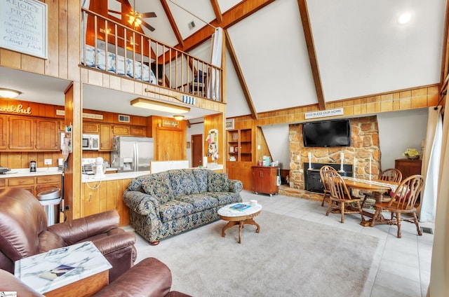 tiled living room featuring a stone fireplace, wood walls, high vaulted ceiling, ceiling fan, and beam ceiling