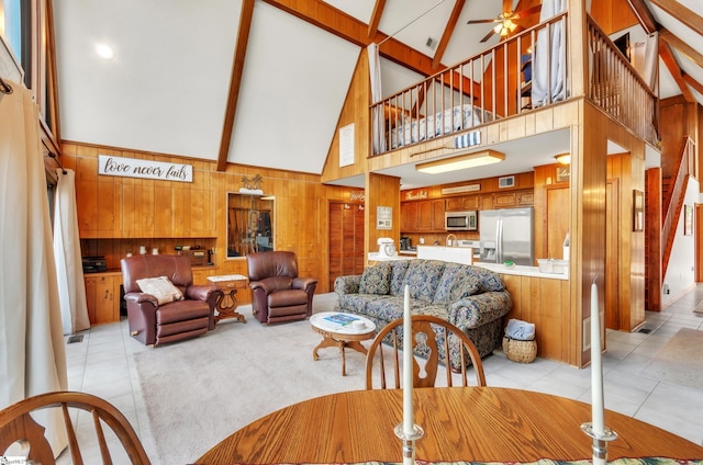 living room with ceiling fan, wooden walls, high vaulted ceiling, and beamed ceiling