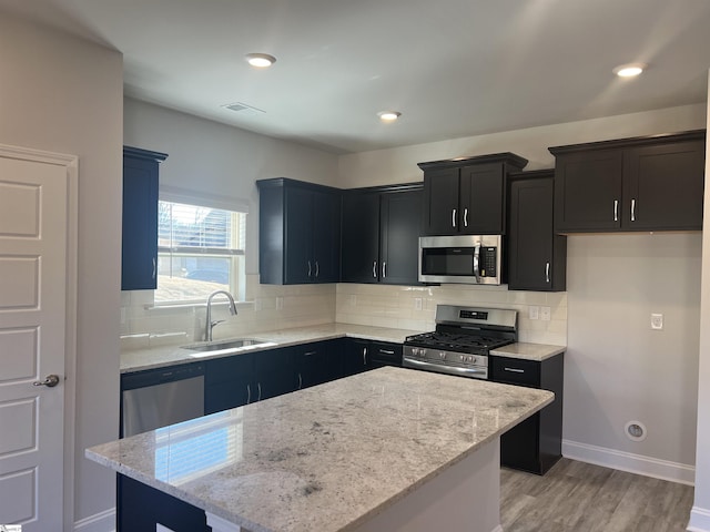 kitchen featuring sink, light stone counters, a kitchen island, stainless steel appliances, and decorative backsplash